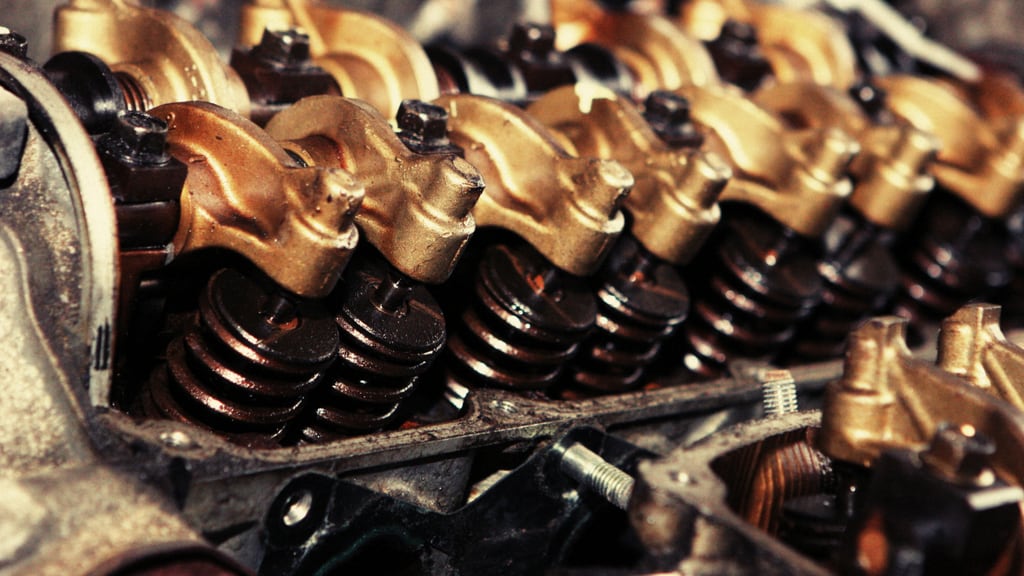 A cylinder head with its bronze rocker arms, valve springs and retainers exposed, with further engine components laid alongside