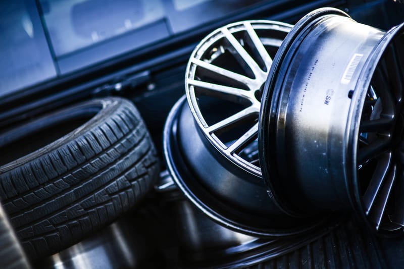 Two bare alloy wheel rims and a loose tyre resting in the load bed of a vehicle