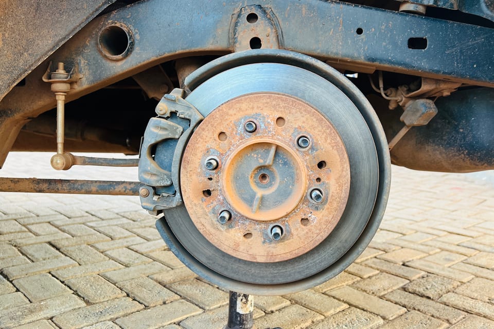 A rusted brake disc, hub and caliper exposed on a car with the wheel removed